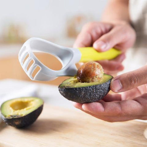 person removing an avocado pip with a grey and green avocado prep tool