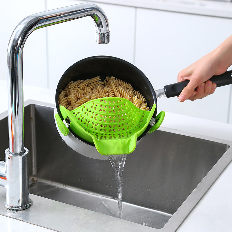 person draining pasta in a sink with a pot and green clip on pot drainer