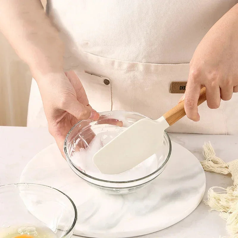 person mixing egg whites in a glass bowl with a white silicone spatula with a wooden handle
