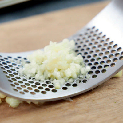 Metallic garlic press with minced garlic on a wooden surface