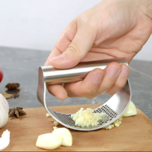 Hand using a garlic press on a wooden cutting board with garlic and peppers.