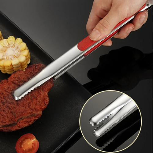 Metal tongs with red handle held over a grill with corn, tomatoes, and meat.