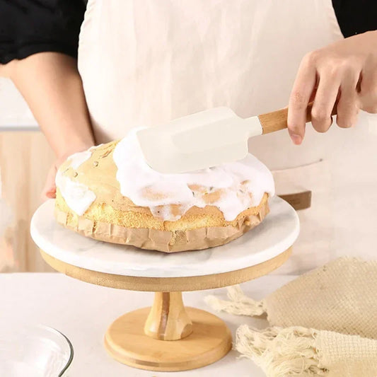person frosting a cake with a white silicone spatula with a wooden handle