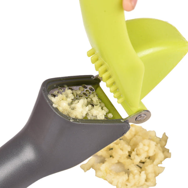 person crushing garlic in a grey garlic press with a green handle