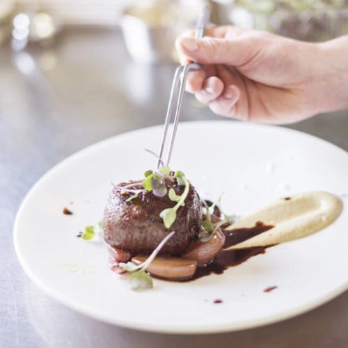 Stainless steel food tweezer tongs garnishing a steak