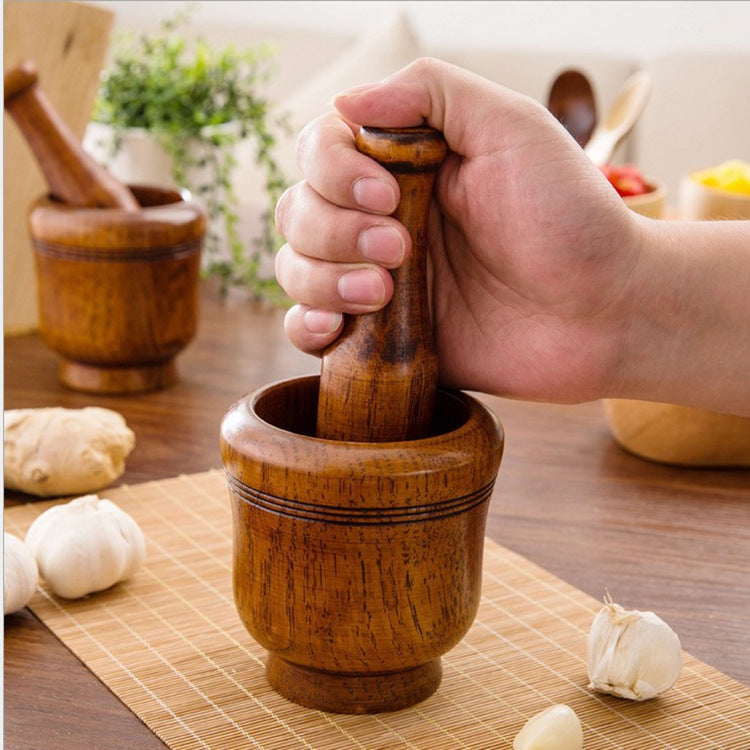 Hand using a wooden mortar and pestle on a table with garlic and ginger.