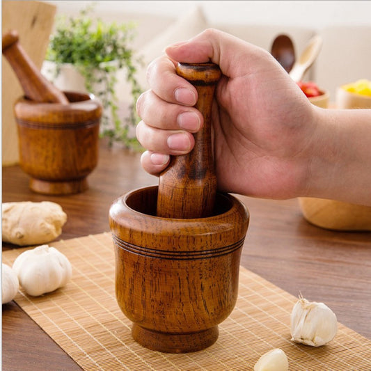 Hand using a wooden mortar and pestle on a table with garlic and ginger.