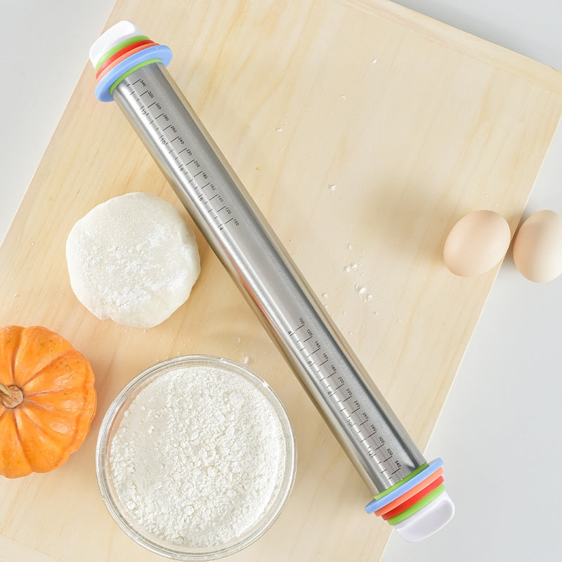 Metal rolling pin with colorful handles on a wooden surface with dough and a small pumpkin.