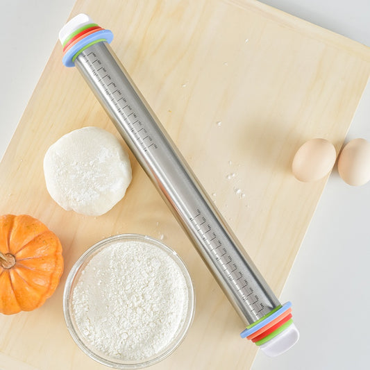Metal rolling pin with colorful handles on a wooden surface with dough and a small pumpkin.