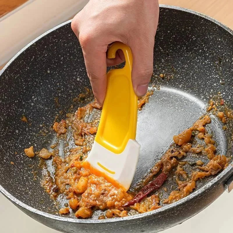 person cleaning a black pan with a yellow and white silicone scraper