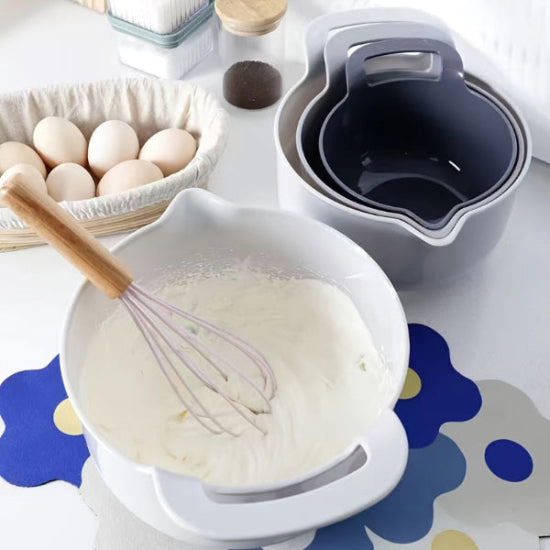 Bowl with whisked ingredients and stacked bowls on a colorful surface