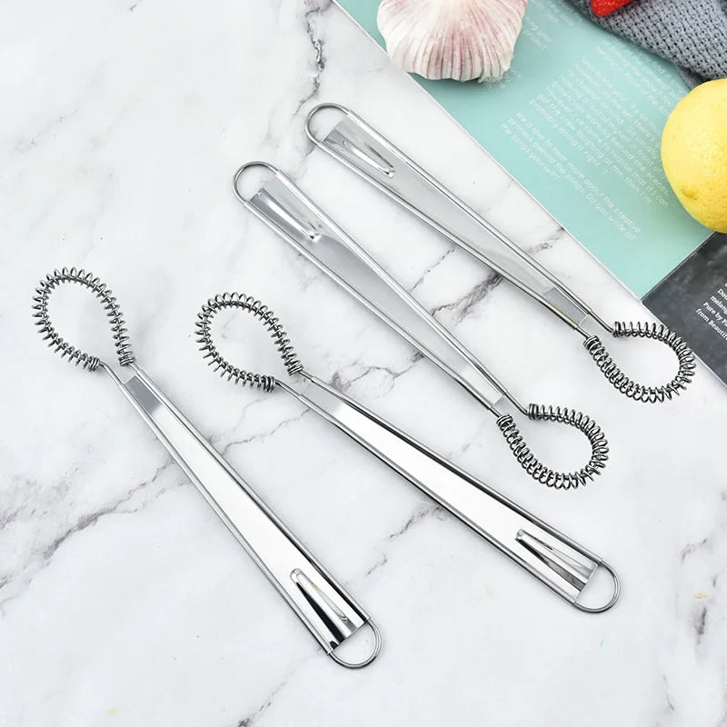 Set of four metal egg whisks on a marble surface