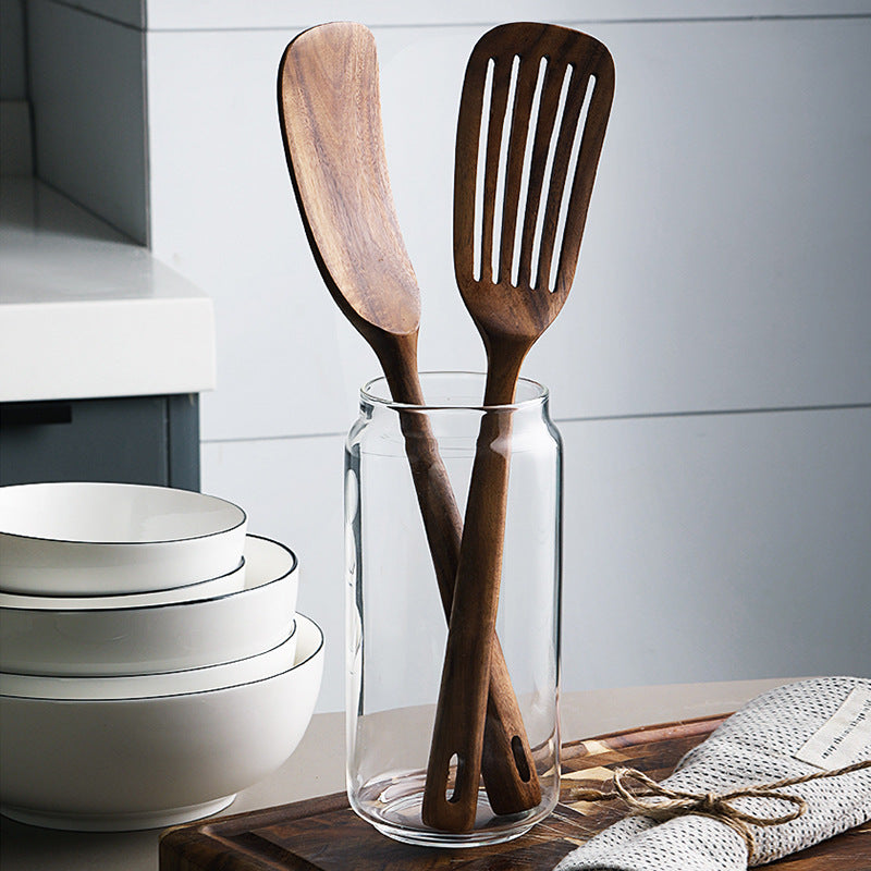 Wooden spatulas in a glass jar with white bowls in the background