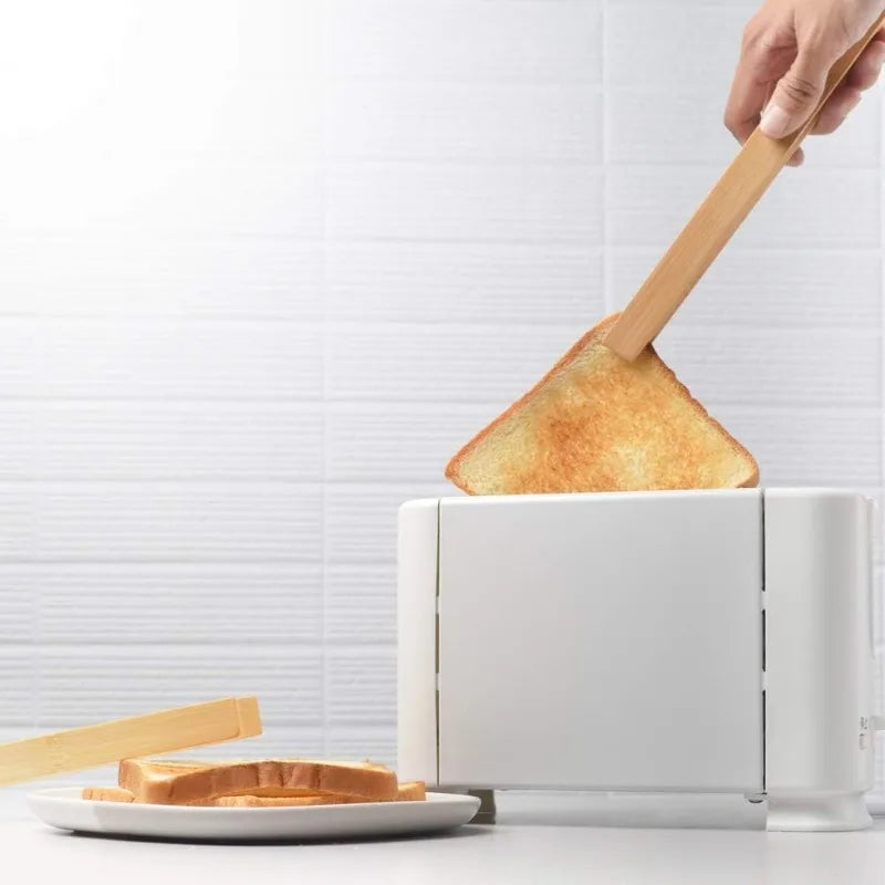 Person using wooden tongs to remove toast from a white toaster with a white background.
