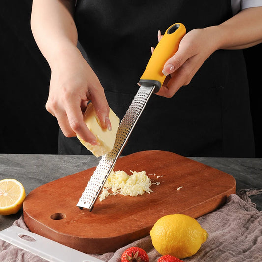 Person using a microplane zester to grate lemon zest on a wooden cutting board with lemons and a knife in the background.